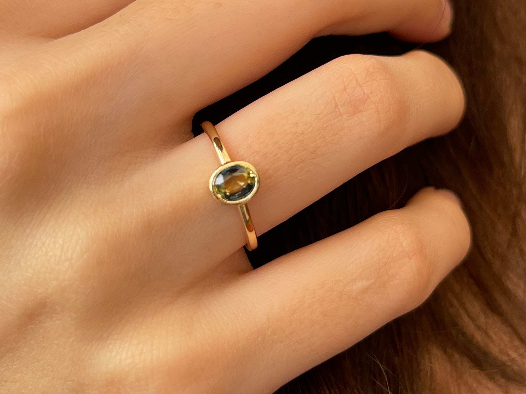 Oval teal petite sapphire gold ring on hand